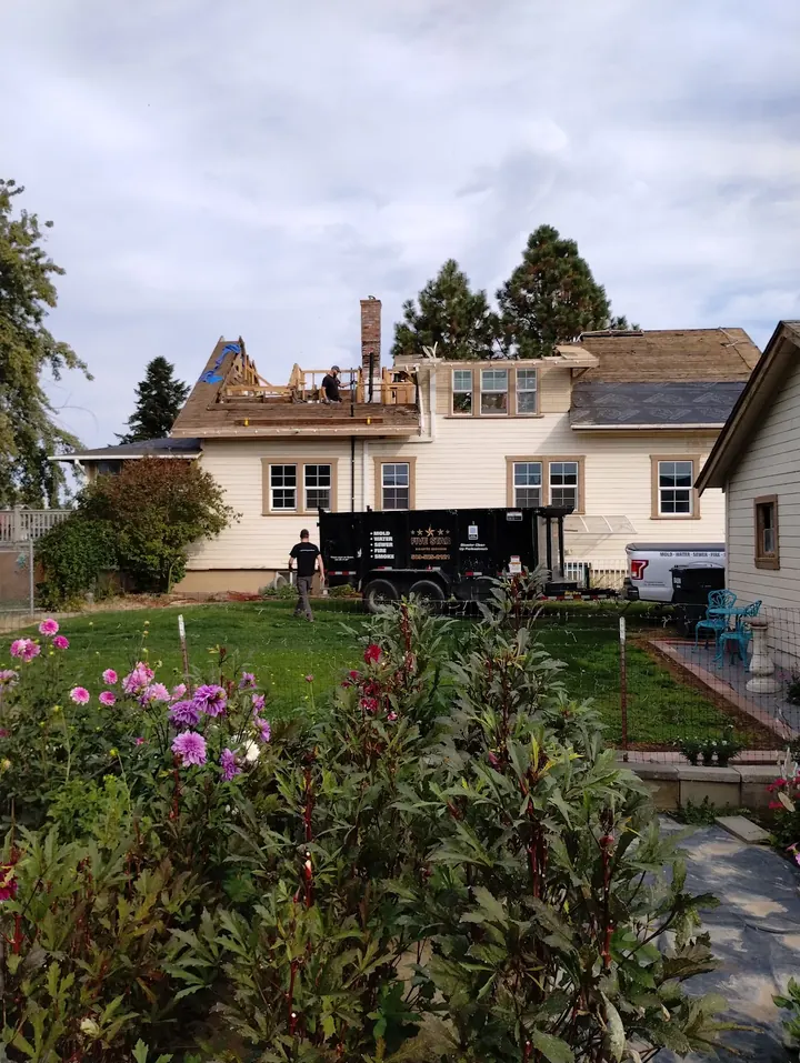 Five Star crew rebuilding the fire-damaged roof framing of a two-story house, with a Five Star dumpster trailer in the yard
