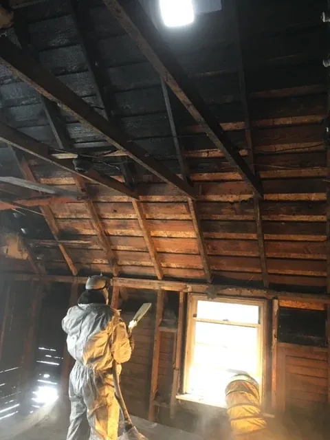 Technician in a protective suit cleaning soot from the charred rafters of an attic